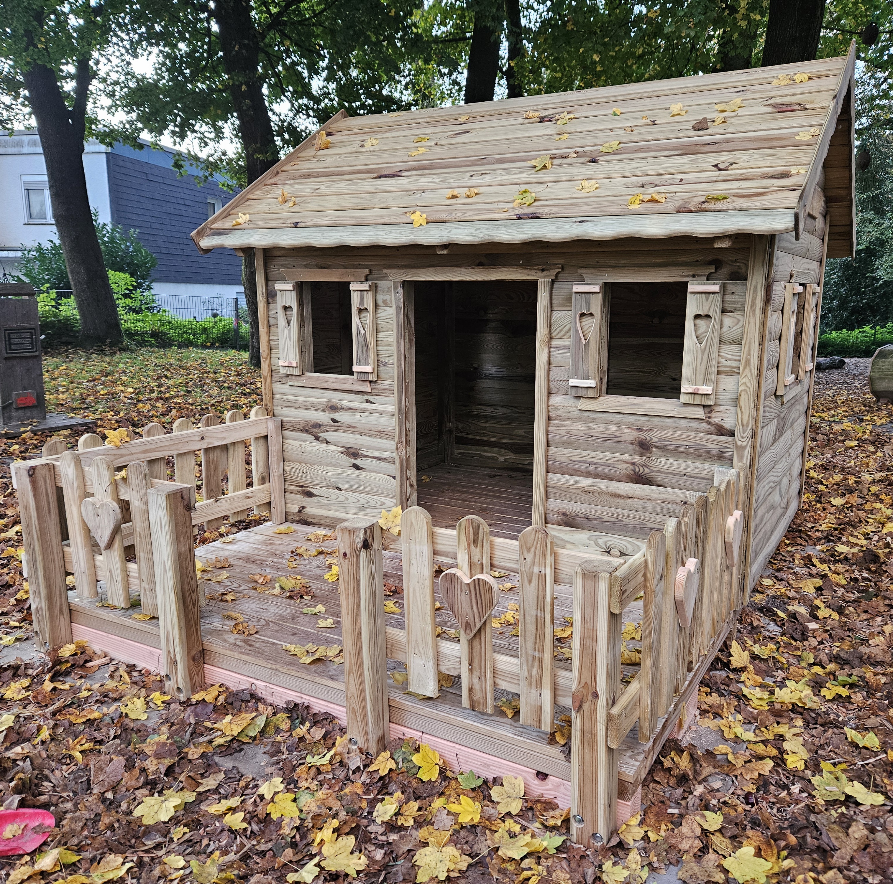 Holzspielhäuschen im Herbstlaub auf dem Kita-Außengelände
